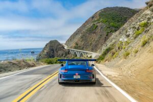 Amalfi Coast Drive Blue sports car drives along a scenic coastal highway, hugging cliffs with the sea in view.